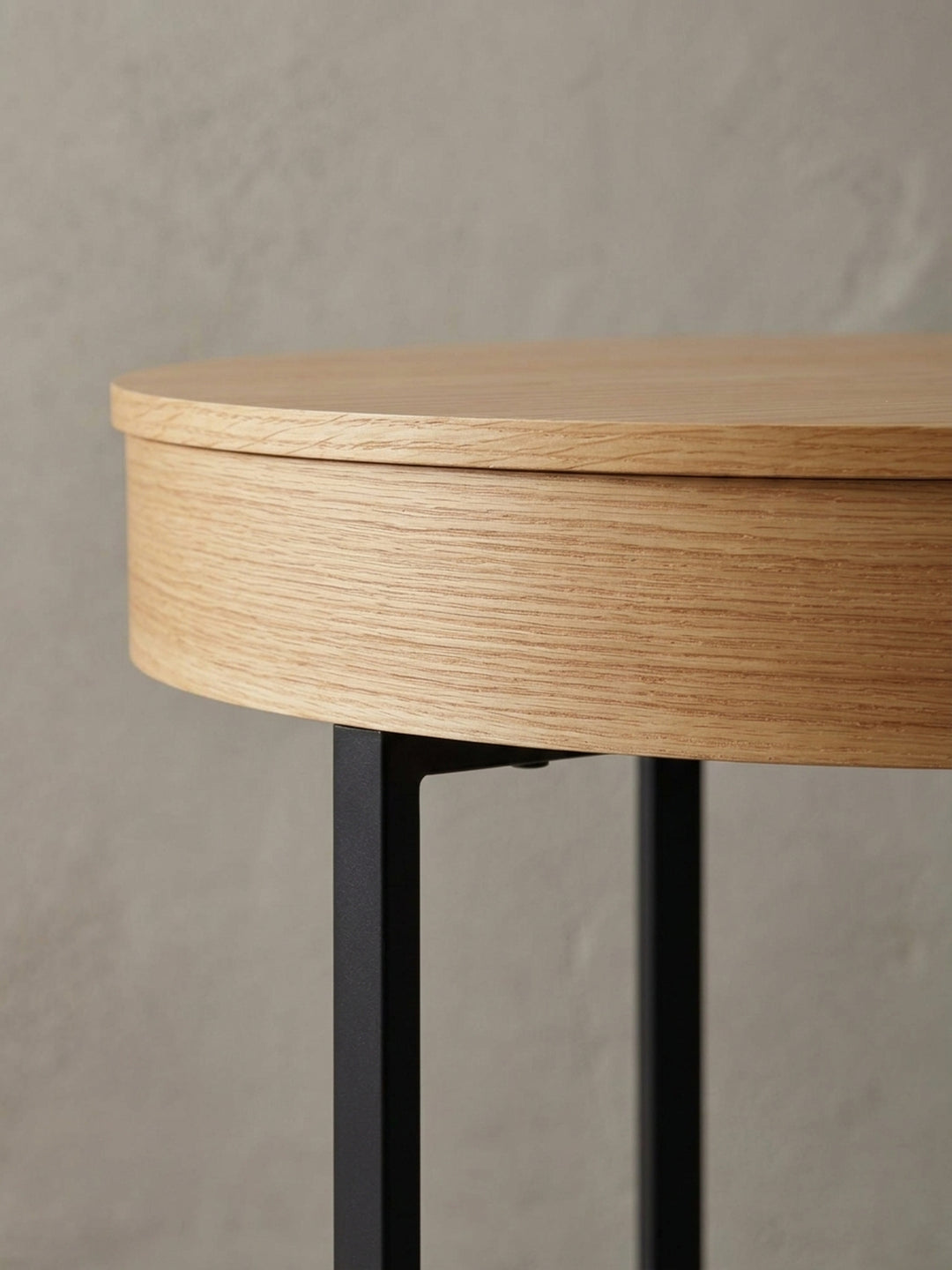 Detailaufnahme des Übergangs von der Eichenfurnier-Tischplatte zum mattschwarzen Stahlbein, die den Materialmix des modernen Lounge-Tisches betont._