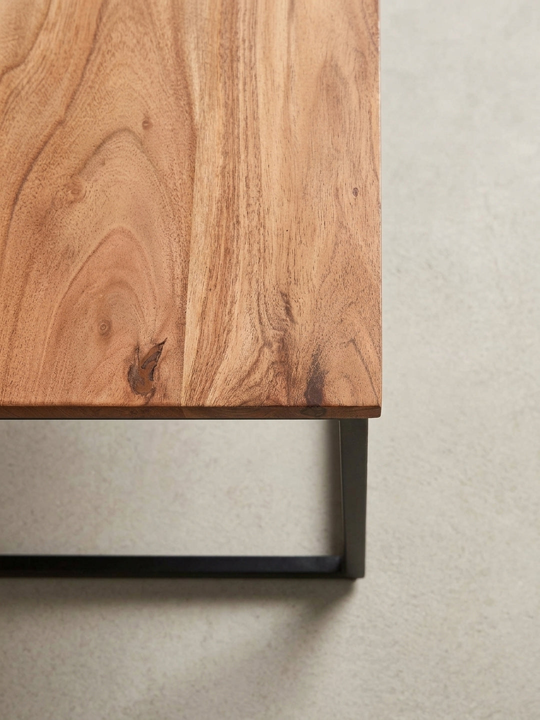 Nahaufnahme der Ecke des Couchtisches, die den präzisen Übergang zwischen der 2 cm dicken Akazienholzplatte und dem robusten 2 cm dicken Metallgestell zeigt._
