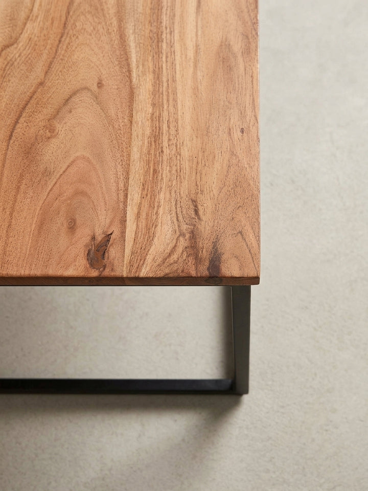 Nahaufnahme der Ecke des Couchtisches, die den präzisen Übergang zwischen der 2 cm dicken Akazienholzplatte und dem robusten 2 cm dicken Metallgestell zeigt._