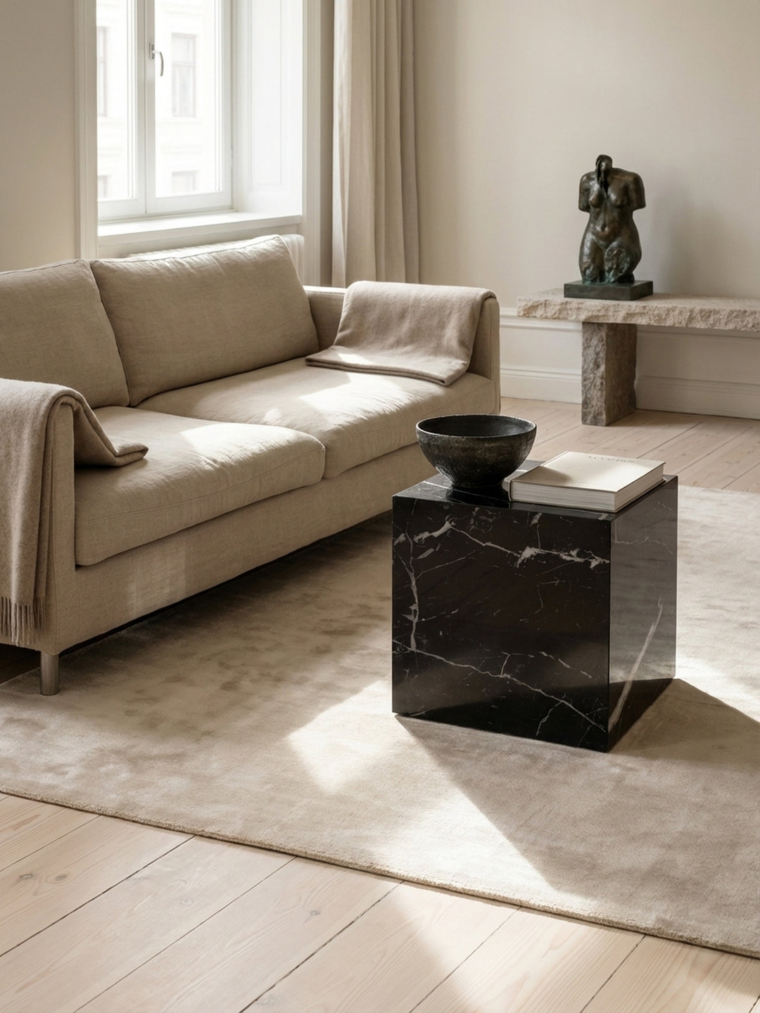 Der schwarze Cube-Wohnzimmertisch kombiniert mit einem beigefarbenen Sofa und einem strukturierten Teppich für ein harmonisches Ambiente._