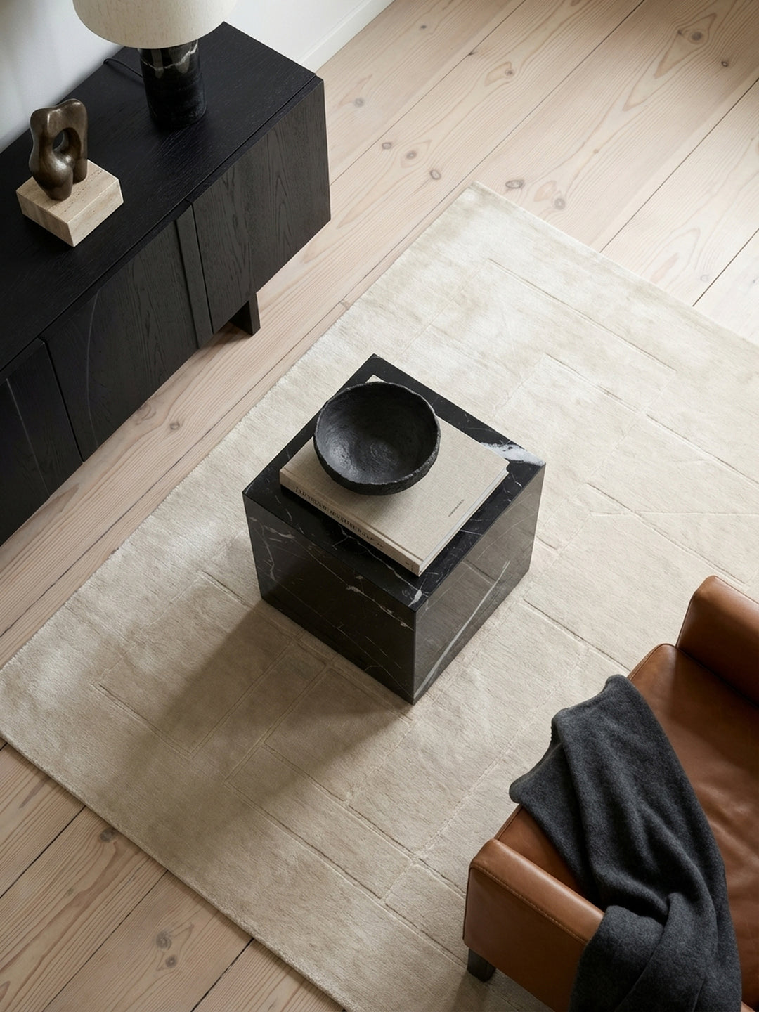 Design Beistelltisch in Würfelform von oben gesehen, arrangiert auf einem hellen Wollteppich neben einer modernen Couch._