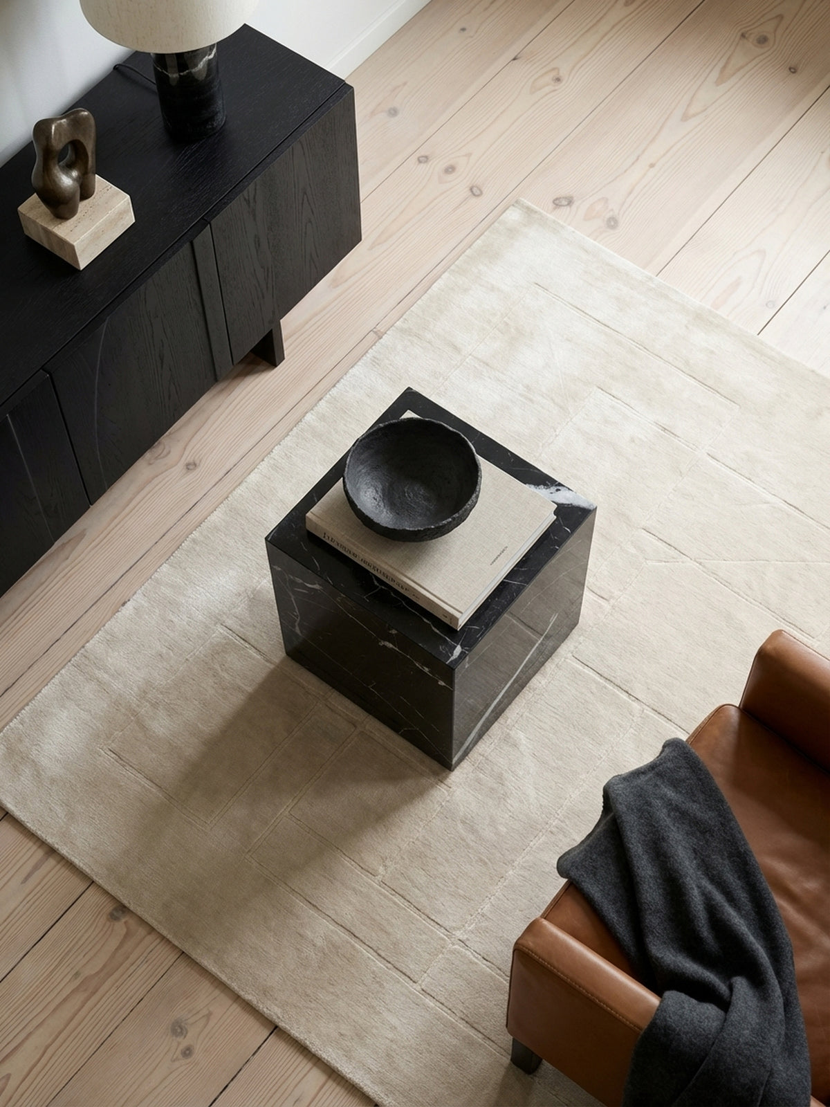 Design Beistelltisch in Würfelform von oben gesehen, arrangiert auf einem hellen Wollteppich neben einer modernen Couch.