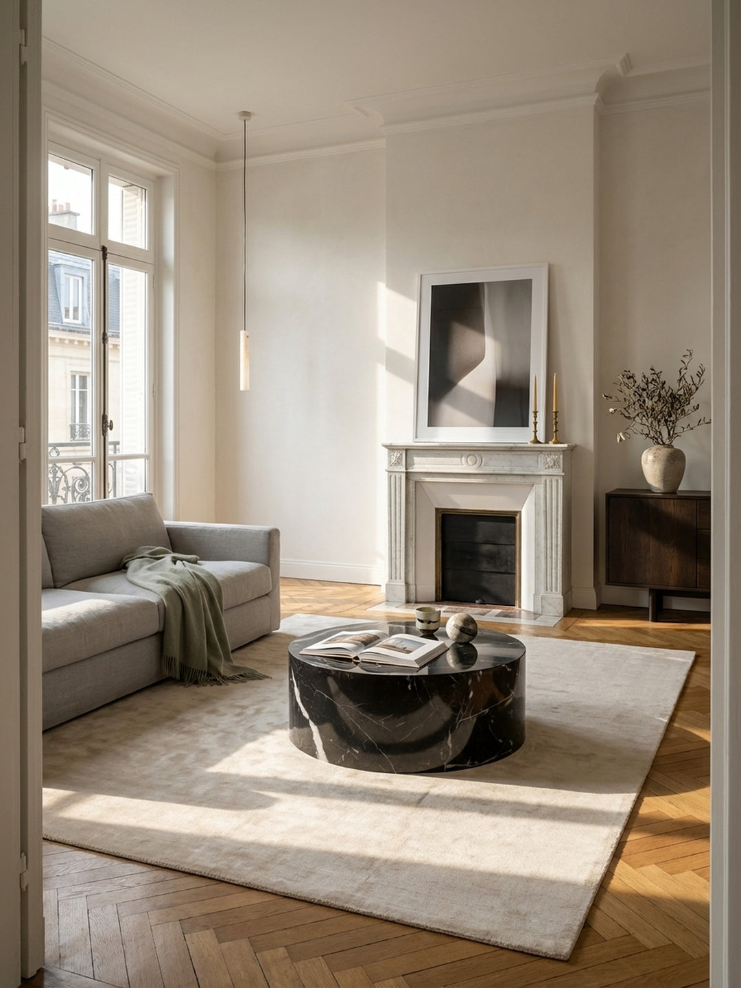 Ein runder Couchtisch in schwarzer Marmoroptik als Herzstück eines eleganten Altbau-Wohnzimmers mit Fischgrätparkett und Stuckdecke._