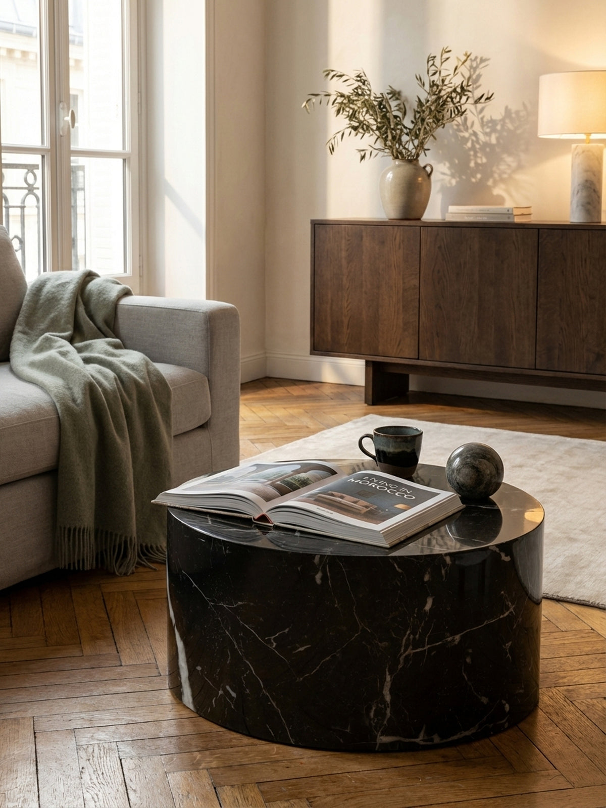 Design-Vignette mit einem offenen Bildband und einem Glas Wasser auf dem modernen, runden Sofatisch in Schwarz-Marmor-Optik.