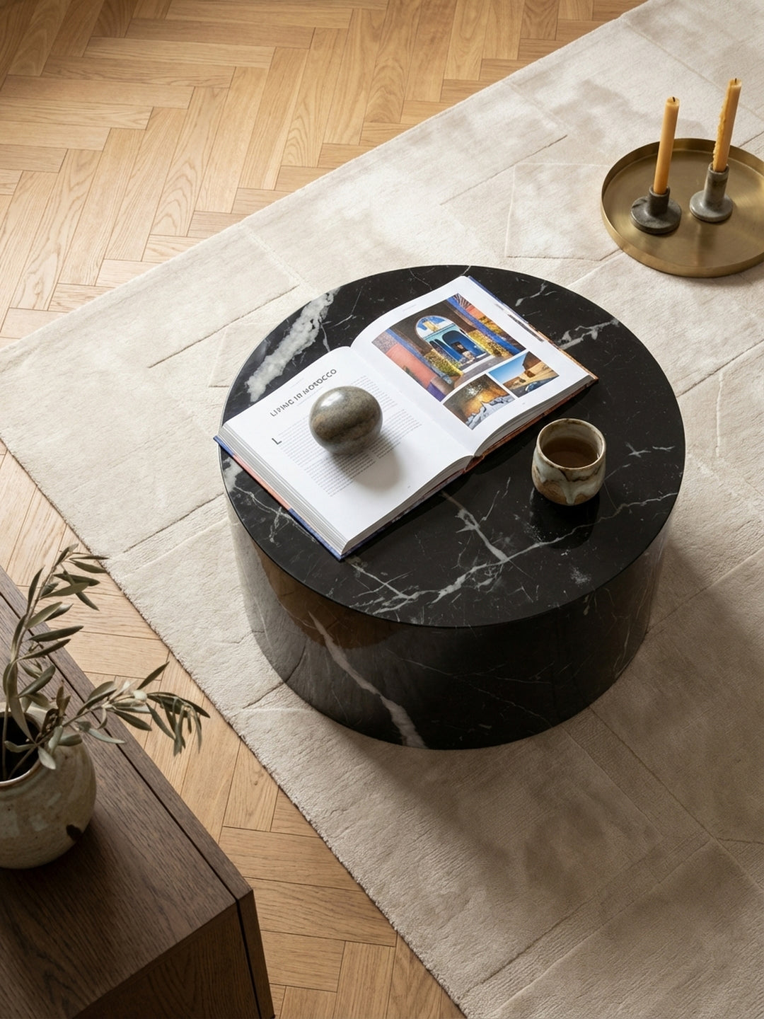 Draufsicht auf den runden Kaffeetisch mit glänzender Oberfläche, platziert auf einem cremefarbenen Wollteppich vor einem grauen Sofa._