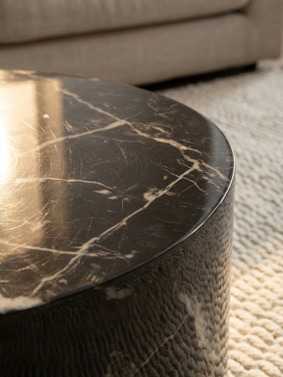 Makroaufnahme der hochglänzenden Oberfläche des Couchtischs, die die feine weiße Maserung der schwarzen Marmor-Optik detailreich zeigt._