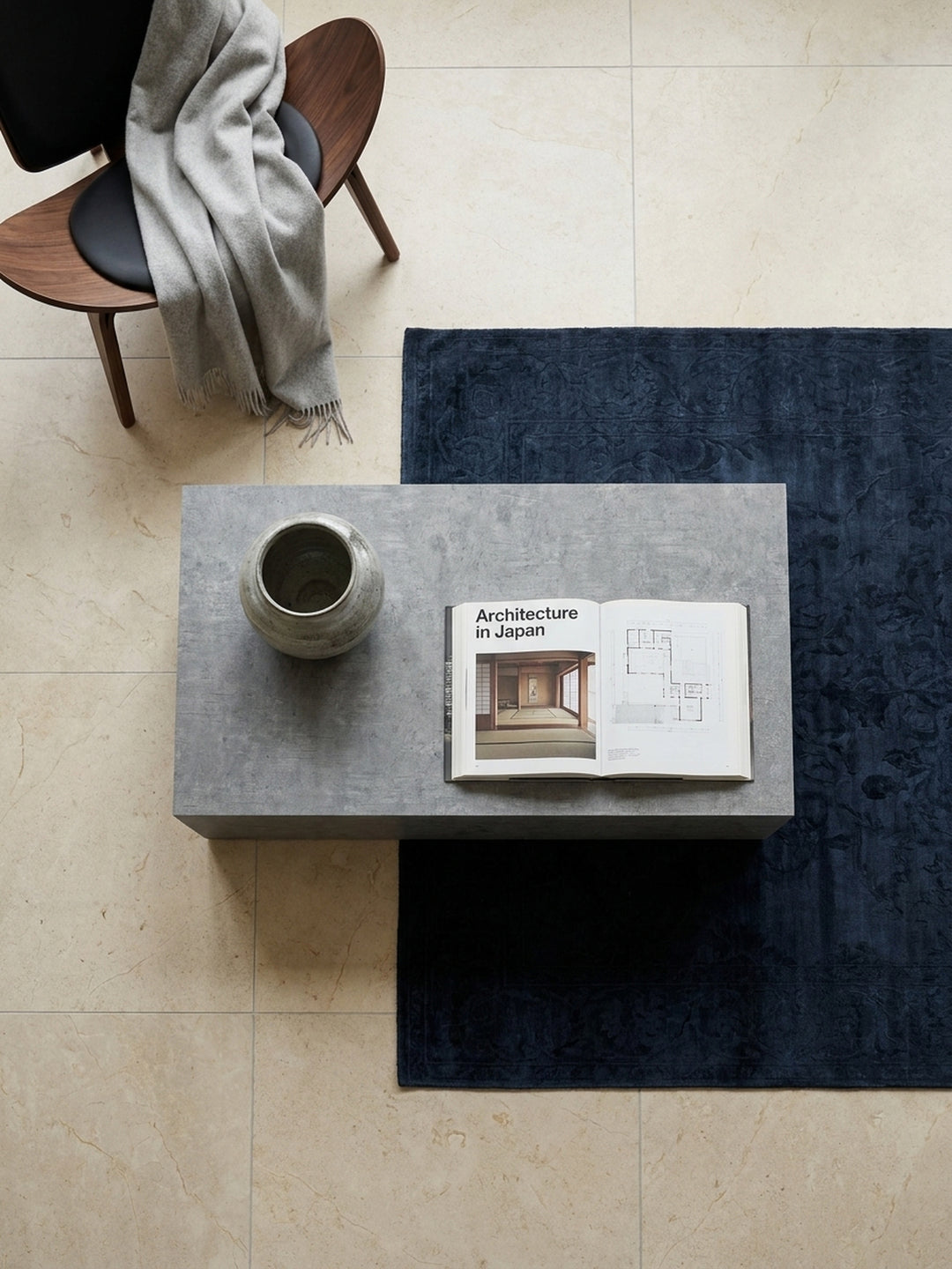 Draufsicht auf einen rechteckigen Wohnzimmertisch im Beton-Design, der symmetrisch auf einem silbergrauen Seidenteppich platziert ist._
