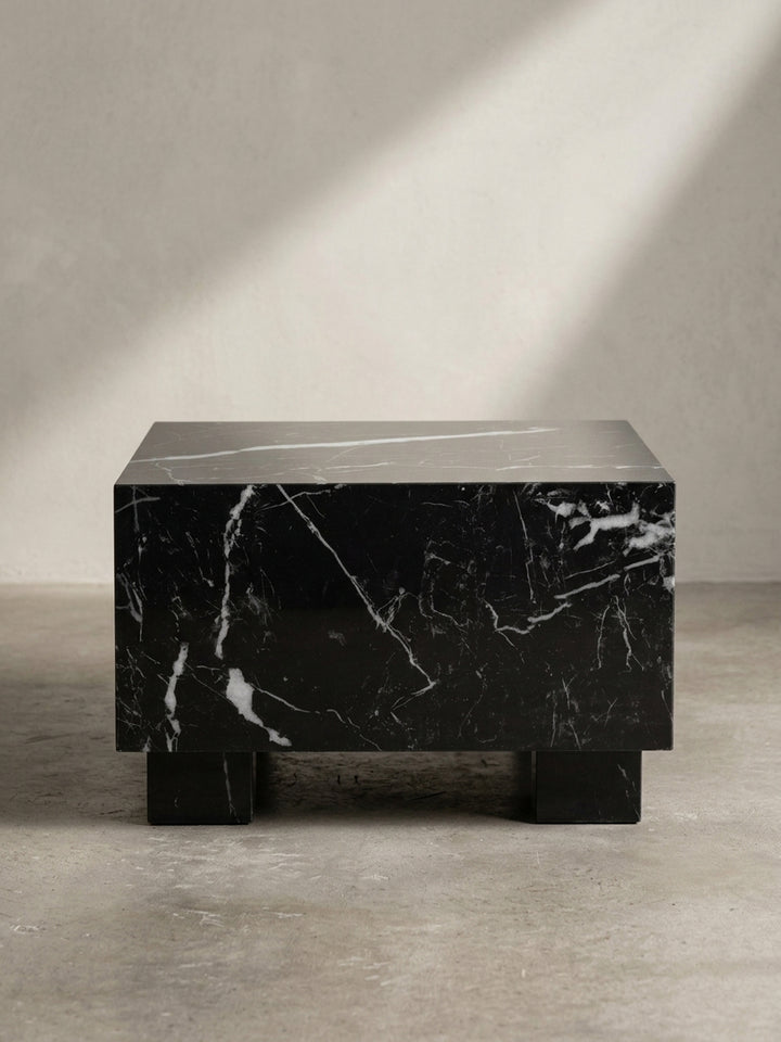 Dreiviertelansicht des quadratischen Design-Sofatisches, die seine geometrische Würfel-Form und die glatte Marmor-Optik hervorhebt._