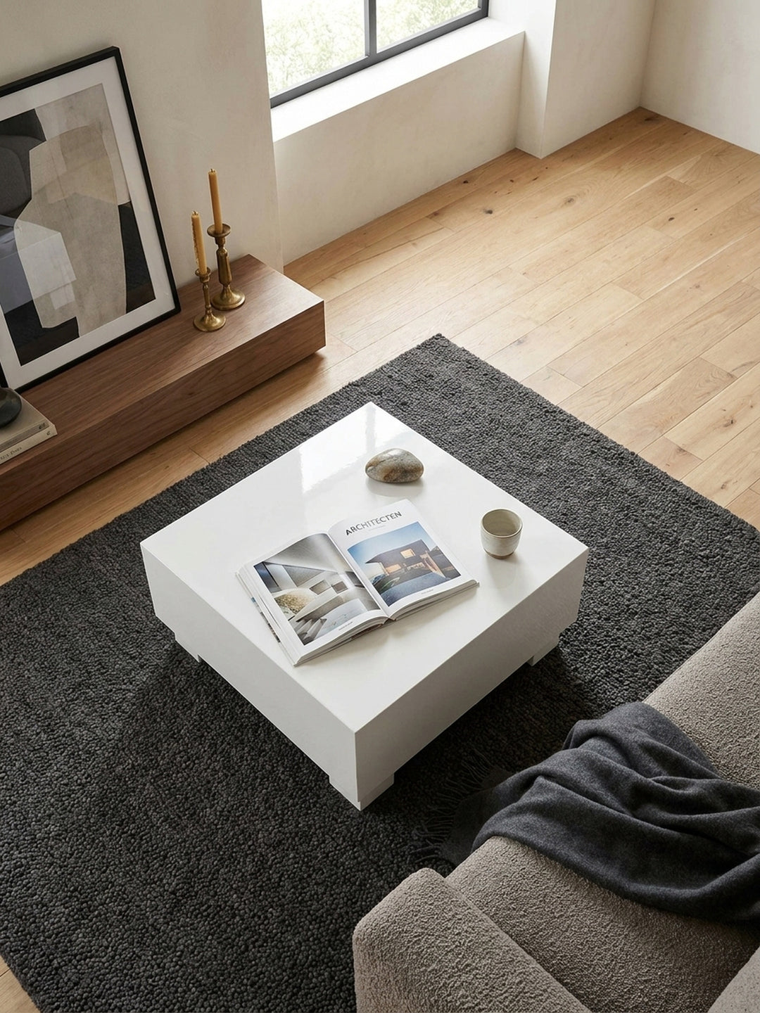 Blick von oben auf den weißen Hochglanz-Couchtisch 60x60x35 cm arrangiert mit Architektur-Bildbänden neben einem Lounge-Sessel._