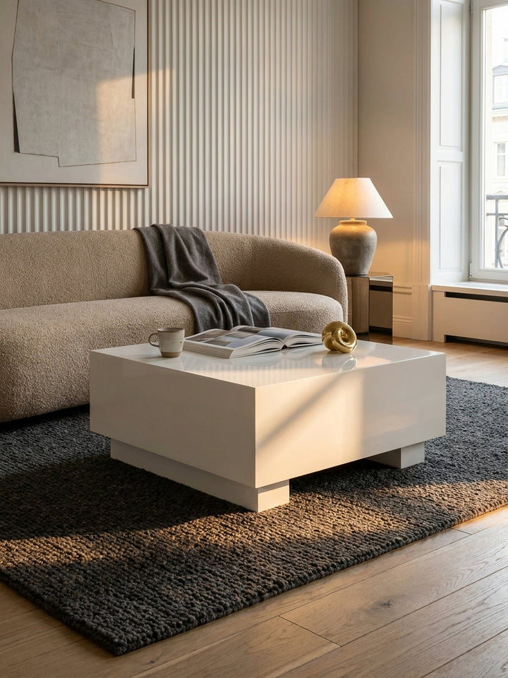 Makroaufnahme der weißen Hochglanzlack-Oberfläche des quadratischen Couchtisches, die weiches Licht reflektiert und glatte Kanten zeigt._