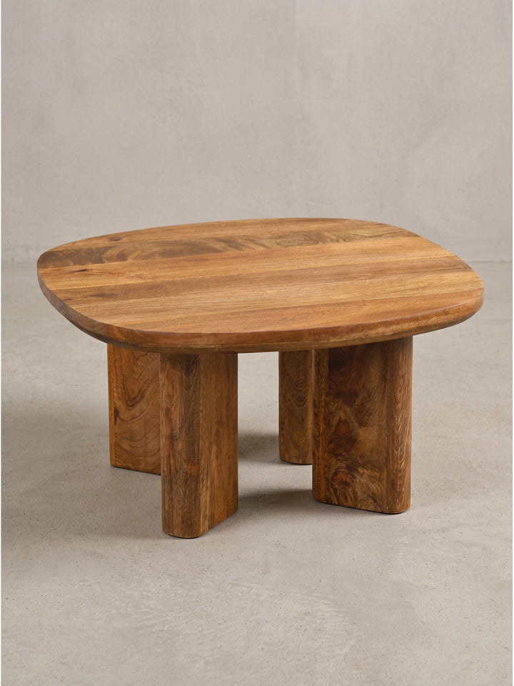 Vorderansicht des massiven Couchtisches aus Mangoholz mit klaren Linien und markanten Säulenbeinen vor sauberem weißen Hintergrund im Fotostudio._