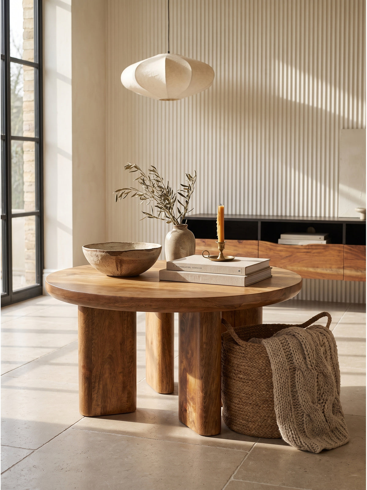 Handgefertigter Holztisch mit stark abgerundeten Kanten, dekoriert mit einer aschegrauen Wabi-Sabi Keramikschale und Leinenbüchern neben einer Travertinlampe._