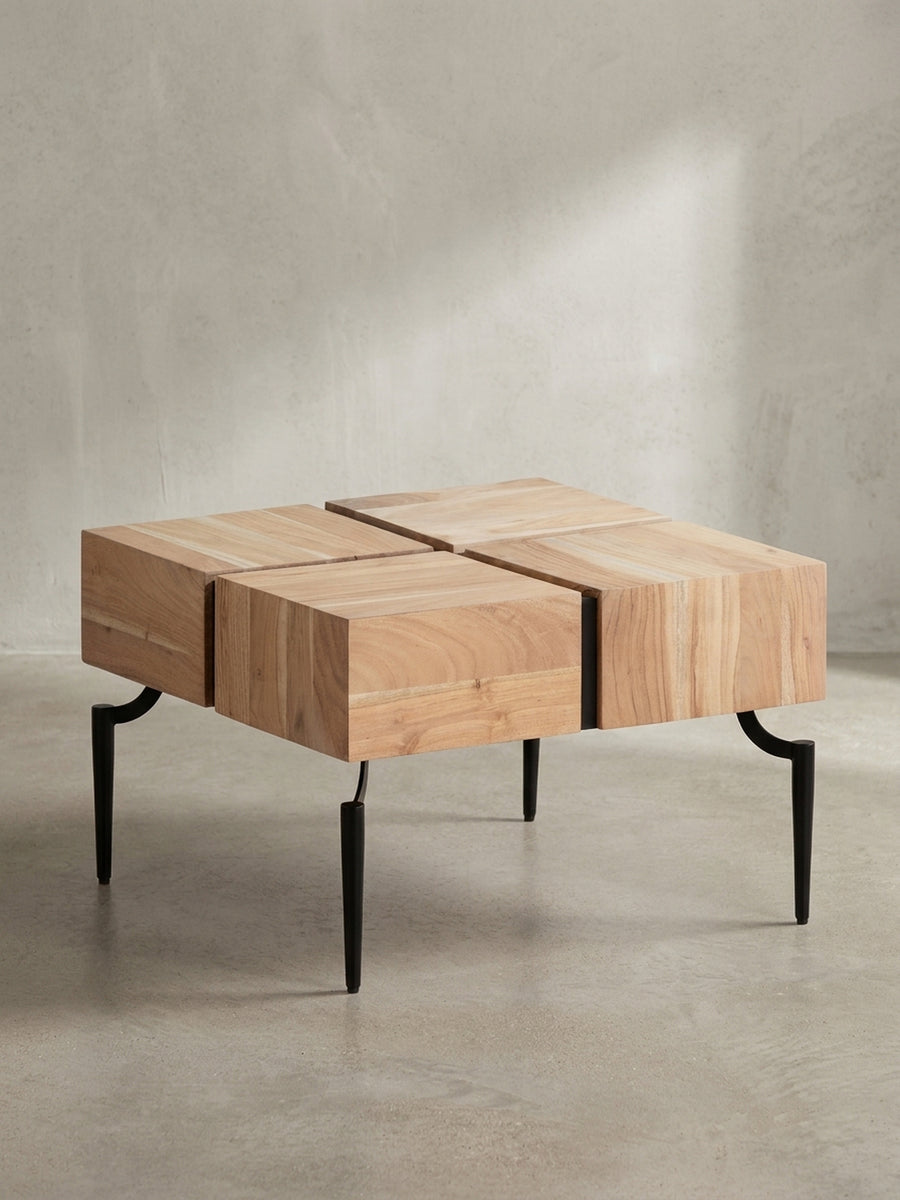 Freigestellte Frontansicht des quadratischen Couchtisches, der sein einzigartiges Design mit vier Akazienholz-Blöcken und filigranen schwarzen Metallbeinen präsentiert._