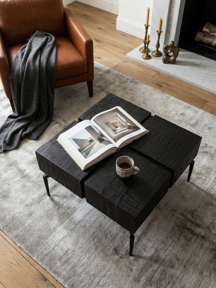 Draufsicht auf den schwarzen Würfel-Couchtisch auf einem hellen Teppich, der die geometrische Anordnung im modernen Wohnzimmer zeigt._