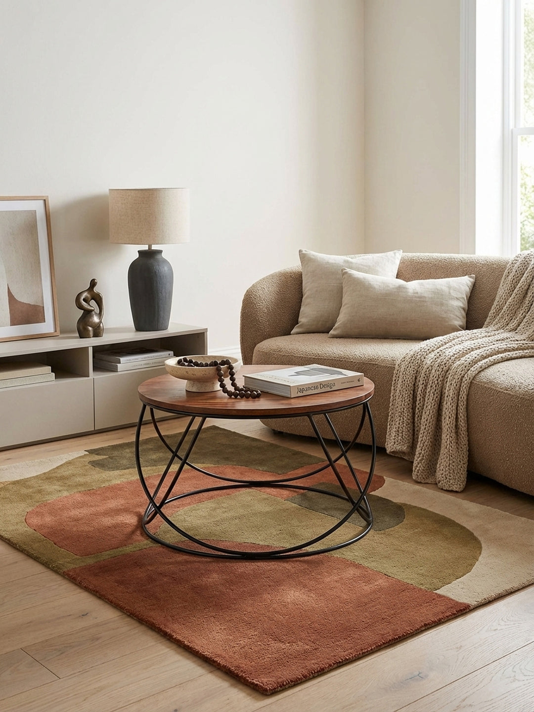 Ein runder Couchtisch aus Sheesham Massivholz mit schwarzem Metallgestell steht in einem hellen Wohnzimmer vor einem beigen Sofa und unterstreicht den Industrial-Stil._