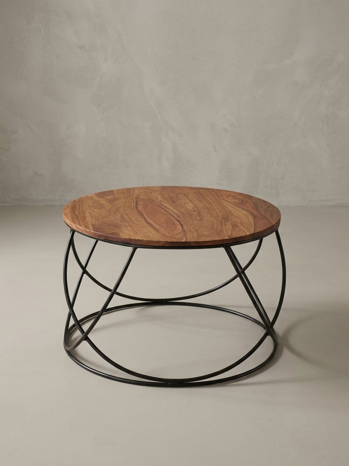 Dreiviertelansicht des Sofatischs im Industrial-Design, der das Zusammenspiel von der warmen Holzplatte und dem skulpturalen, korbförmigen Metallgestell betont._