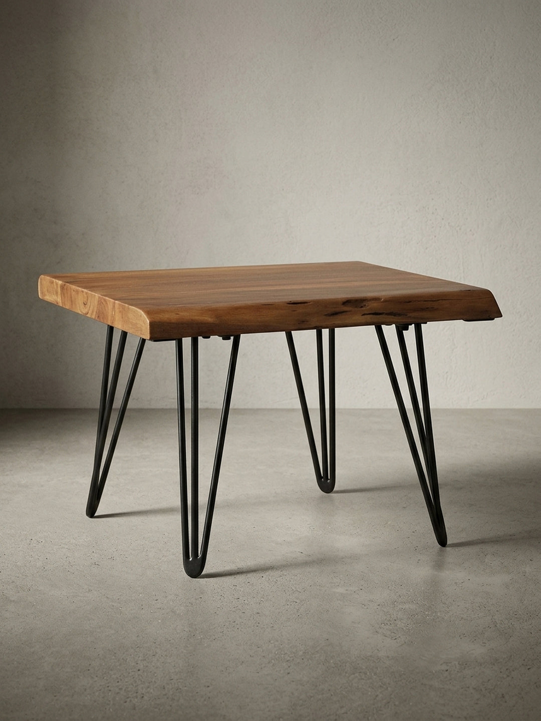 Freigestellter Design Couchtisch aus Massivholz in der Frontansicht. Der kompakte Holztisch zeigt seine natürliche Baumkante und grazile, schwarze Haarnadelbeine aus Metall._