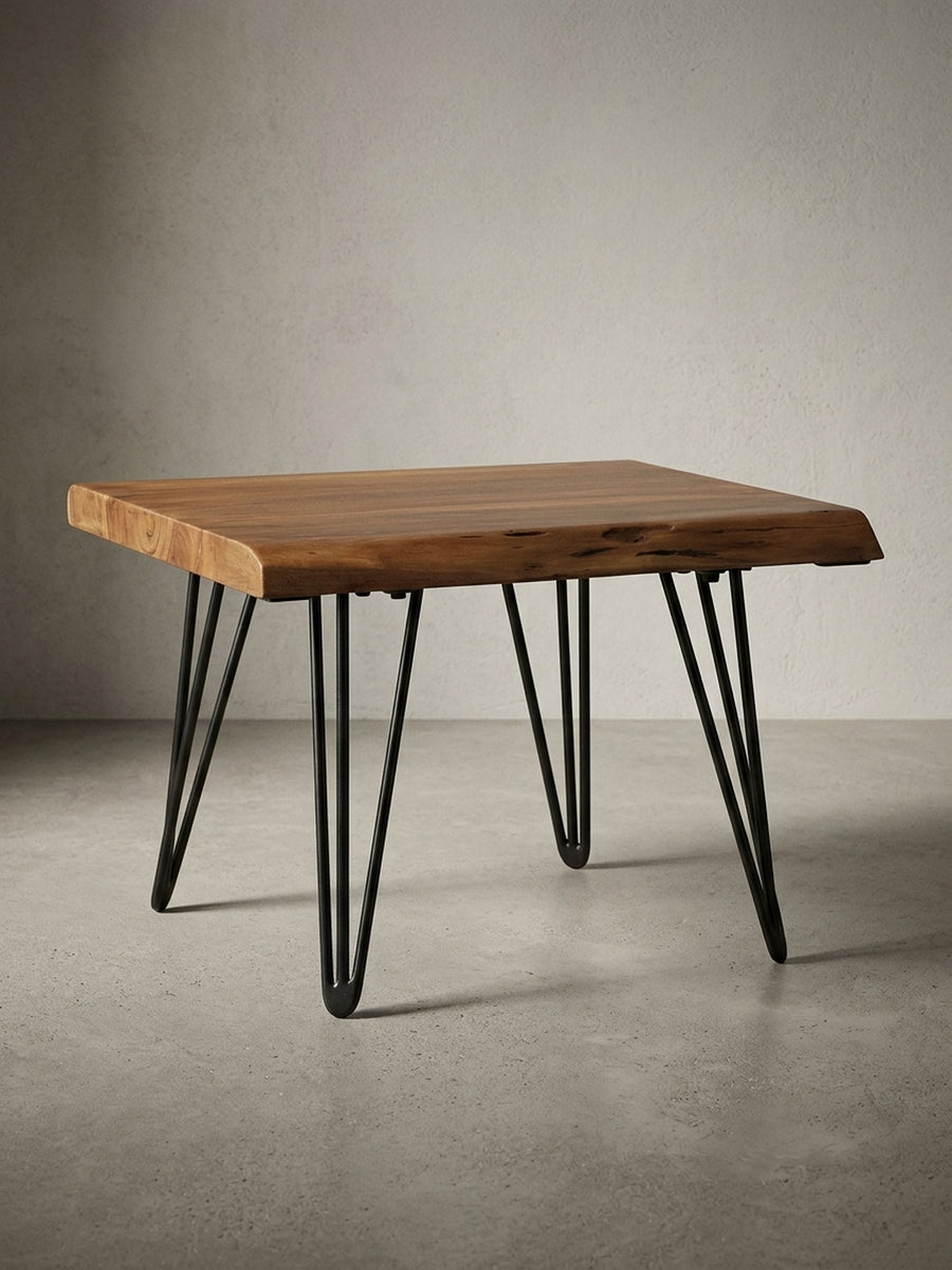 Freigestellter Design Couchtisch aus Massivholz in der Frontansicht. Der kompakte Holztisch zeigt seine natürliche Baumkante und grazile, schwarze Haarnadelbeine aus Metall._