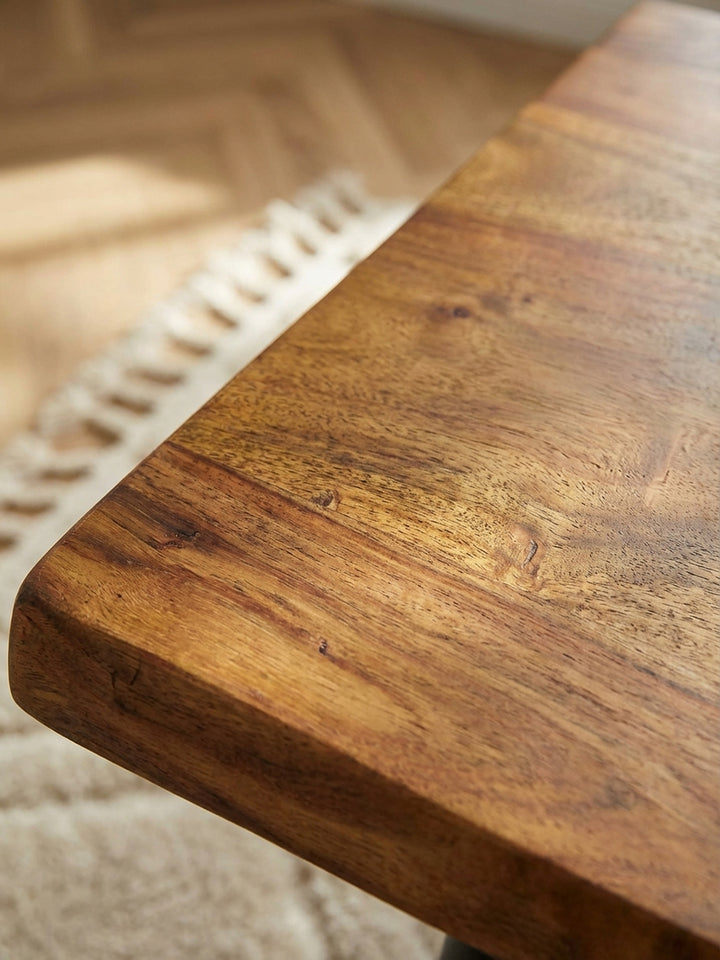 Detailaufnahme der lebendigen Maserung und der natürlichen Baumkante des Massivholz-Couchtischs, die Handwerkskunst und Qualität zeigt._