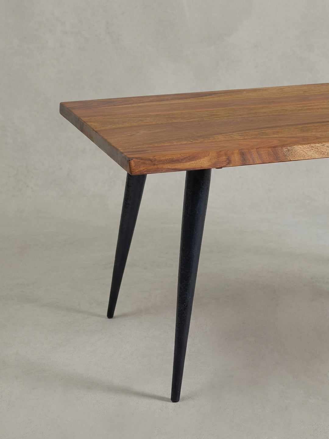 Nahaufnahme eines schlanken, schwarzen Tischbeins und der massiven Holzecke, die den Kontrast zwischen industriellem Design und Naturmaterial verdeutlicht._