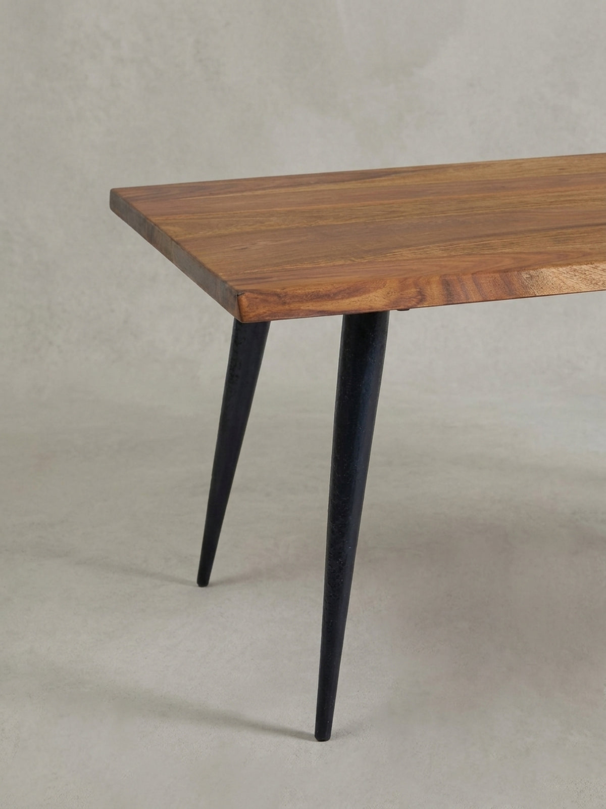 Nahaufnahme eines schlanken, schwarzen Tischbeins und der massiven Holzecke, die den Kontrast zwischen industriellem Design und Naturmaterial verdeutlicht._