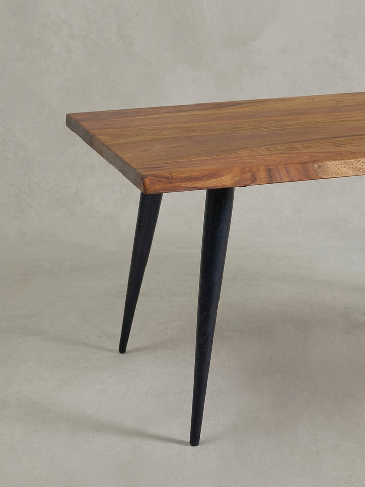 Nahaufnahme eines schlanken, schwarzen Tischbeins und der massiven Holzecke, die den Kontrast zwischen industriellem Design und Naturmaterial verdeutlicht._