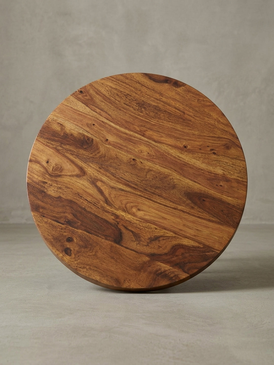 Alternativer Blickwinkel auf den runden Kaffeetisch, der die dynamische Holzmaserung der Sheesham-Platte und das moderne Design des schwarzen Metallgestells hervorhebt._
