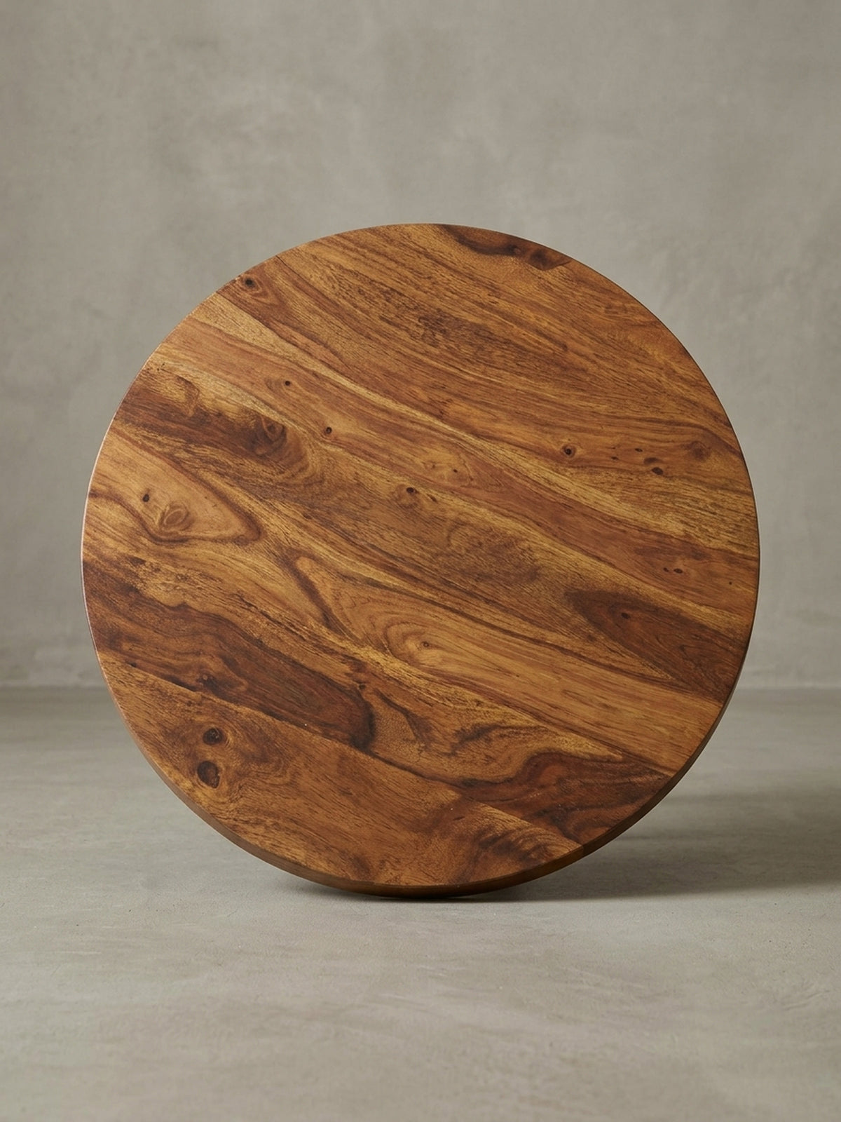 Alternativer Blickwinkel auf den runden Kaffeetisch, der die dynamische Holzmaserung der Sheesham-Platte und das moderne Design des schwarzen Metallgestells hervorhebt._
