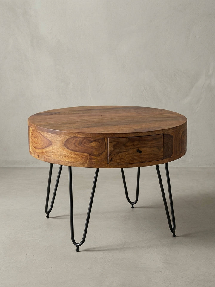 Runder Couchtisch Sheesham Massivholz auf weißem Hintergrund. Der kompakte Wohnzimmertisch besticht durch seinen zylindrischen Korpus und die feinen schwarzen Metallbeine._