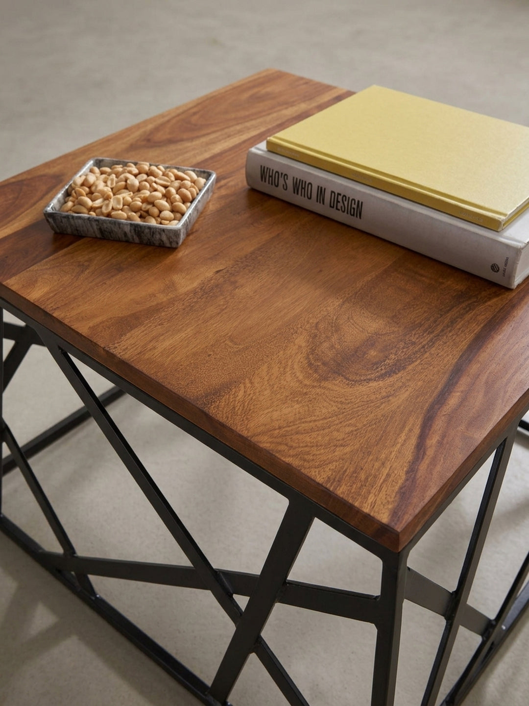 Weitere Perspektive des Kaffeetisches freigestellt vor Weiß. Die asymmetrische Anordnung der Eisenstreben macht den quadratischen Massivholztisch zum Blickfang vor der Sofalandschaft._