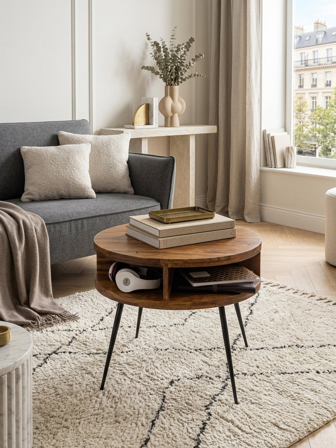 Draufsicht auf den runden Massivholz-Couchtisch im Wohnzimmer. Die markante Holzmaserung der 60cm Tischplatte und die geometrische Ablage wirken im modernen Interieur elegant._