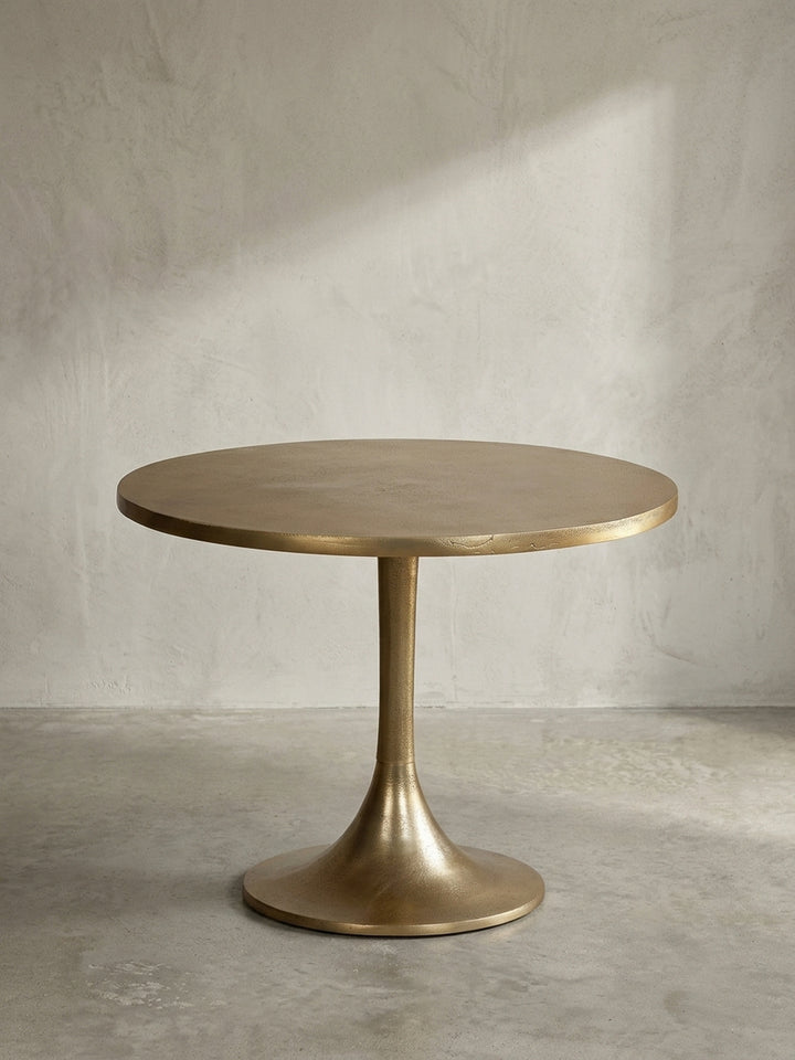 Freigestellter goldener Designtisch aus Aluminium mit rundem Trompetenfuß, Frontalansicht der skulpturalen Silhouette auf weißem Hintergrund._