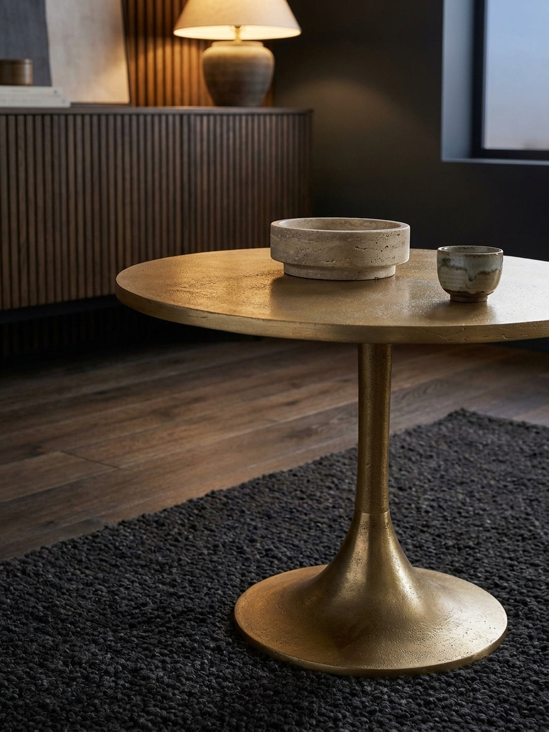 Goldener Beistelltisch mit einem offenen Designmagazin und einer Glasvase, schafft eine stilvolle Leseecke neben einem gemütlichen Sessel._