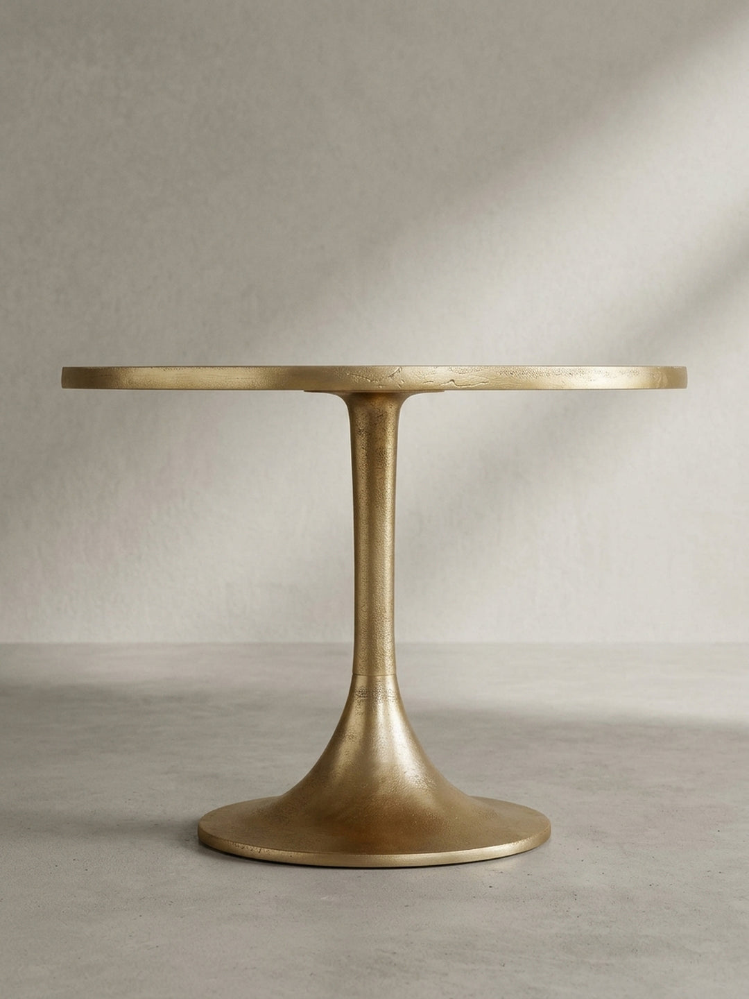 Runder Sofatisch in mattem Gold aus einer schrägen Dreiviertelansicht, die die elegante Verbindung von Tischplatte und Standfuß zeigt._