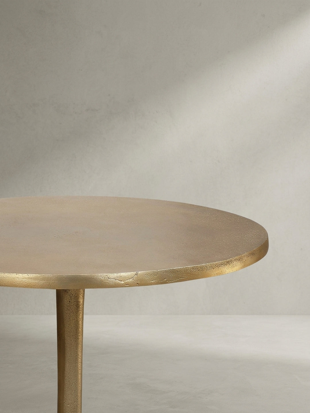 Skulpturaler Anstelltisch in Gold, aus einer leicht erhöhten Perspektive fotografiert, um die runde Tischplatte und die matte Oberfläche zu betonen._