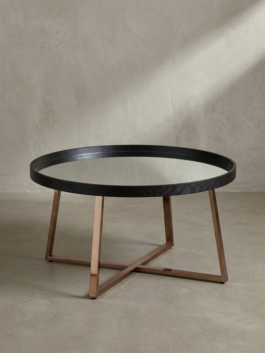 Leicht erhöhte Perspektive auf den runden Design Tisch die den Kontrast zwischen tiefschwarzer Einfassung und reflektierendem Glas betont._
