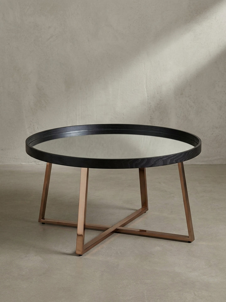 Leicht erhöhte Perspektive auf den runden Design Tisch die den Kontrast zwischen tiefschwarzer Einfassung und reflektierendem Glas betont._
