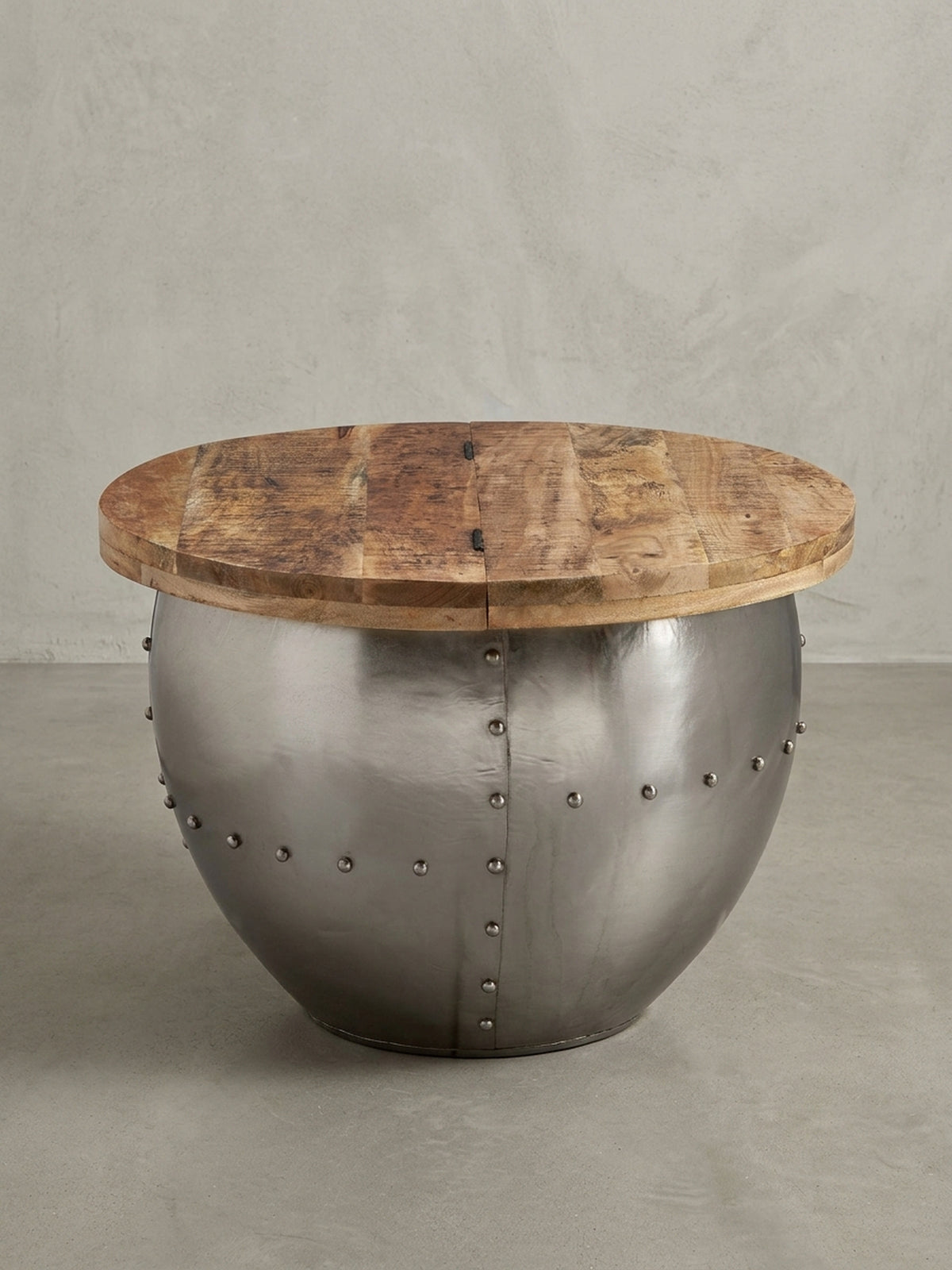 Freigestellter Industrial Couchtisch mit runder Mangoholzplatte und silbernem Metallkorpus mit Nieten, Frontalansicht auf weißem Hintergrund.