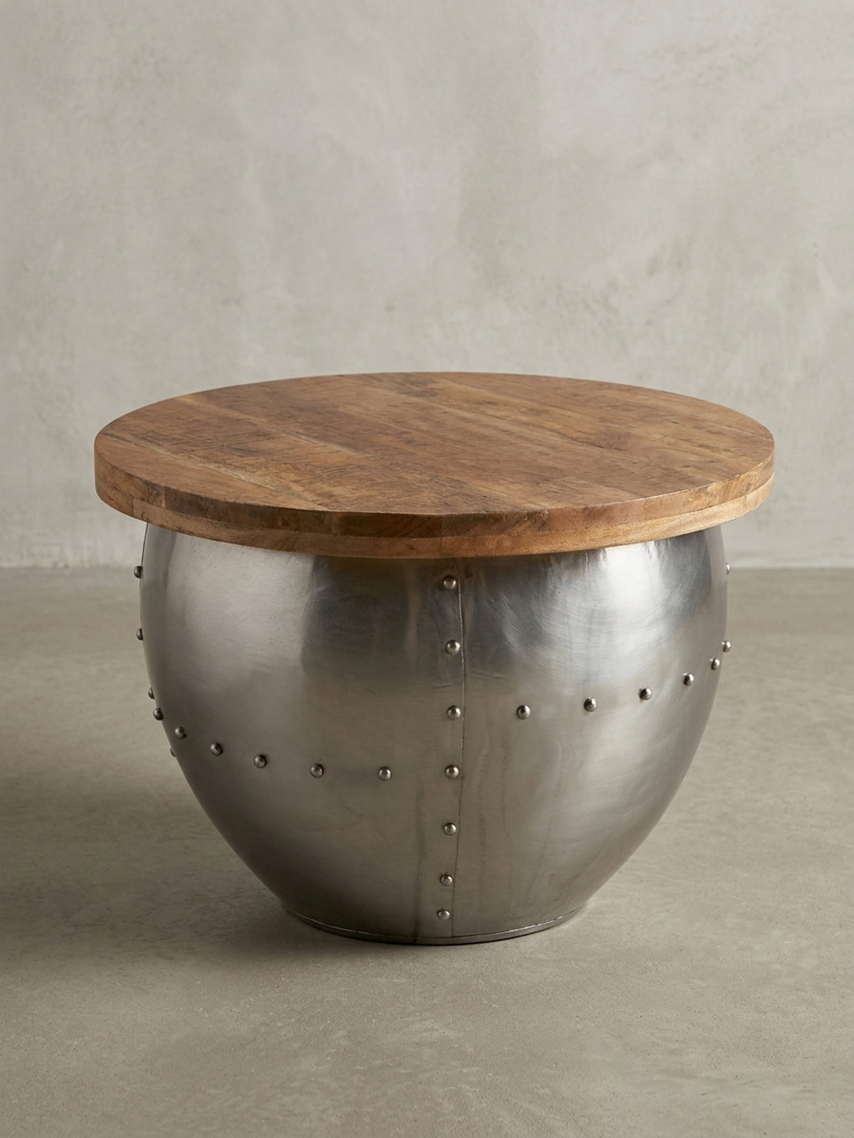 Design Wohnzimmertisch in 3/4-Ansicht, der den Kontrast zwischen dem warmen Massivholz und dem kühlen, genieteten Metallgestell zeigt._