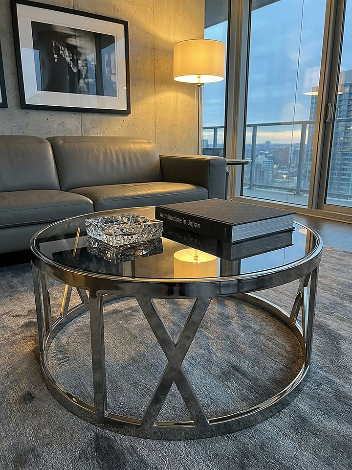 Schwarzes Architekturbuch und Kristallglas auf einem 60x60x30 cm großen Couchtisch im modernen Wohnbereich vor einer rauen Sichtbetonwand._