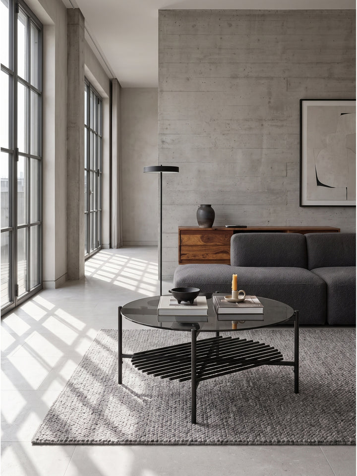 Schwarzer Metall-Couchtisch mit Ablagefläche kombiniert mit einem hellgrauen Loungesofa und einem Beistelltisch aus Beton in einer minimalistischen Raumsituation._