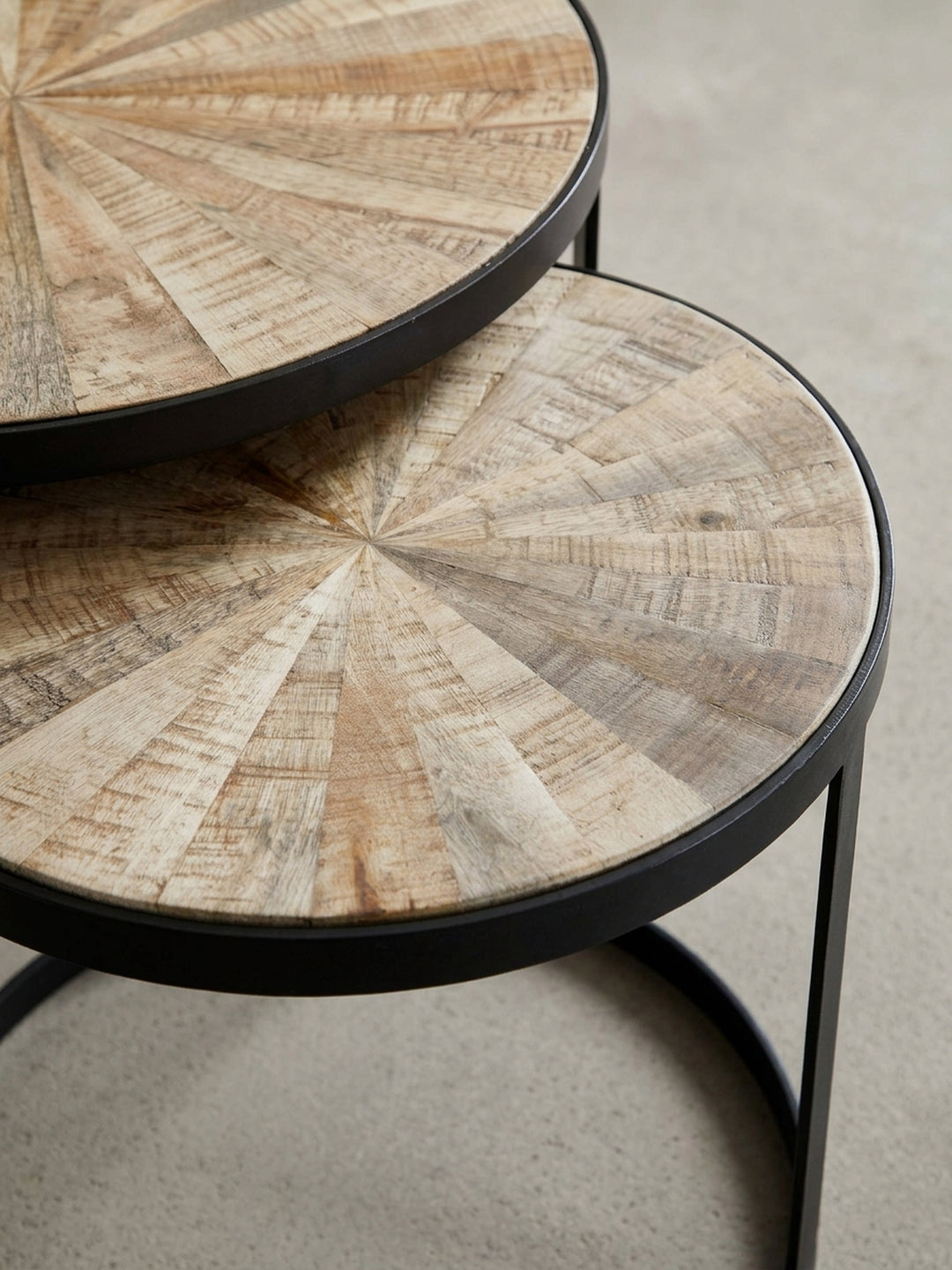 Alternative Perspektive auf den runden Satztisch aus Mango, die das Zusammenspiel von heller Holzoberfläche und dem dunklen, pulverbeschichteten Eisengestell betont._