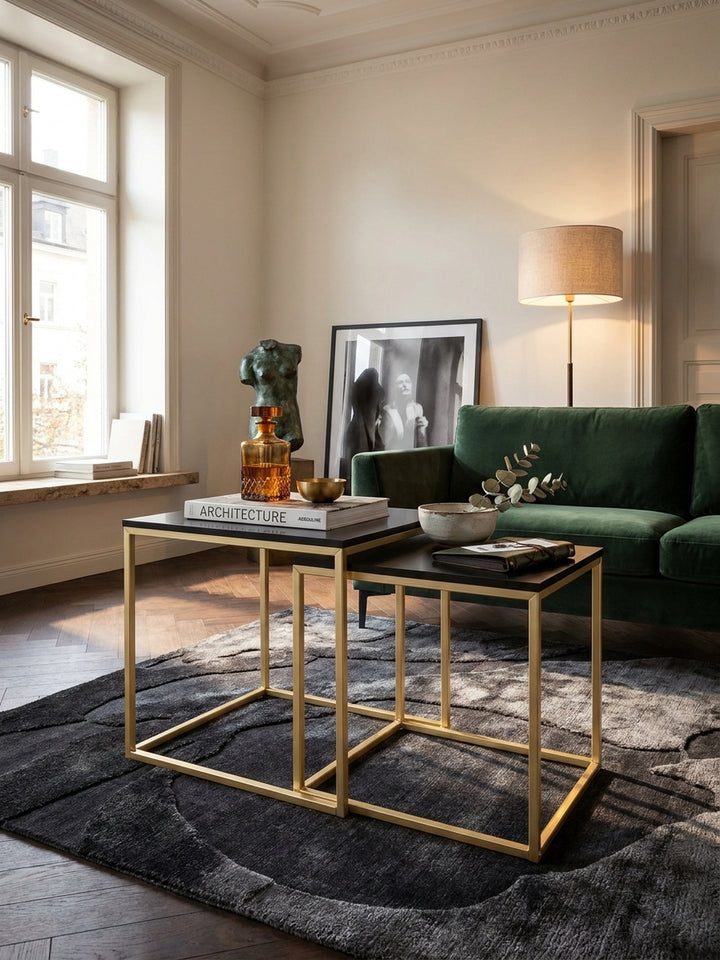 Die matt lackierte schwarze MDF-Oberfläche des Wohnzimmertisches ruht exakt auf dem gold lackierten Vierkant-Metallrahmen im warmen Licht einer Stehlampe._