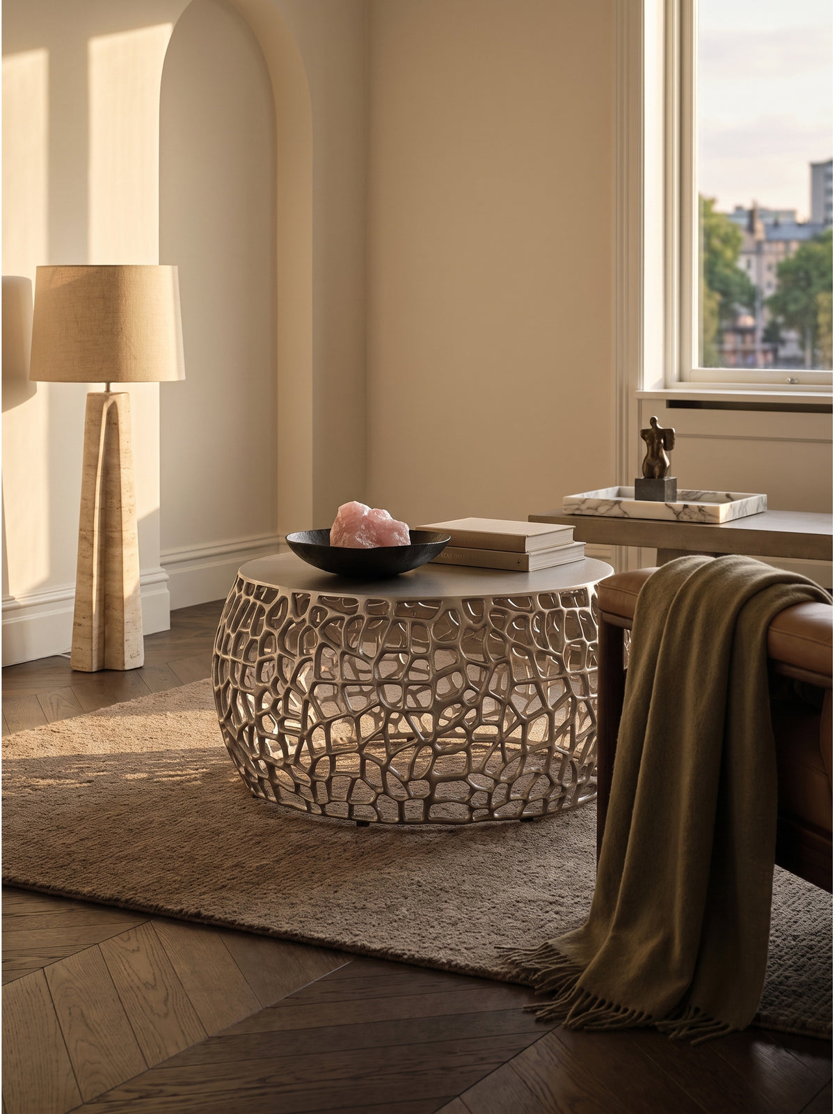 Silberner Metall-Couchtisch 60 cm Durchmesser kombiniert mit einem sandfarbenen Sofa und einer skulpturalen Travertin-Stehlampe