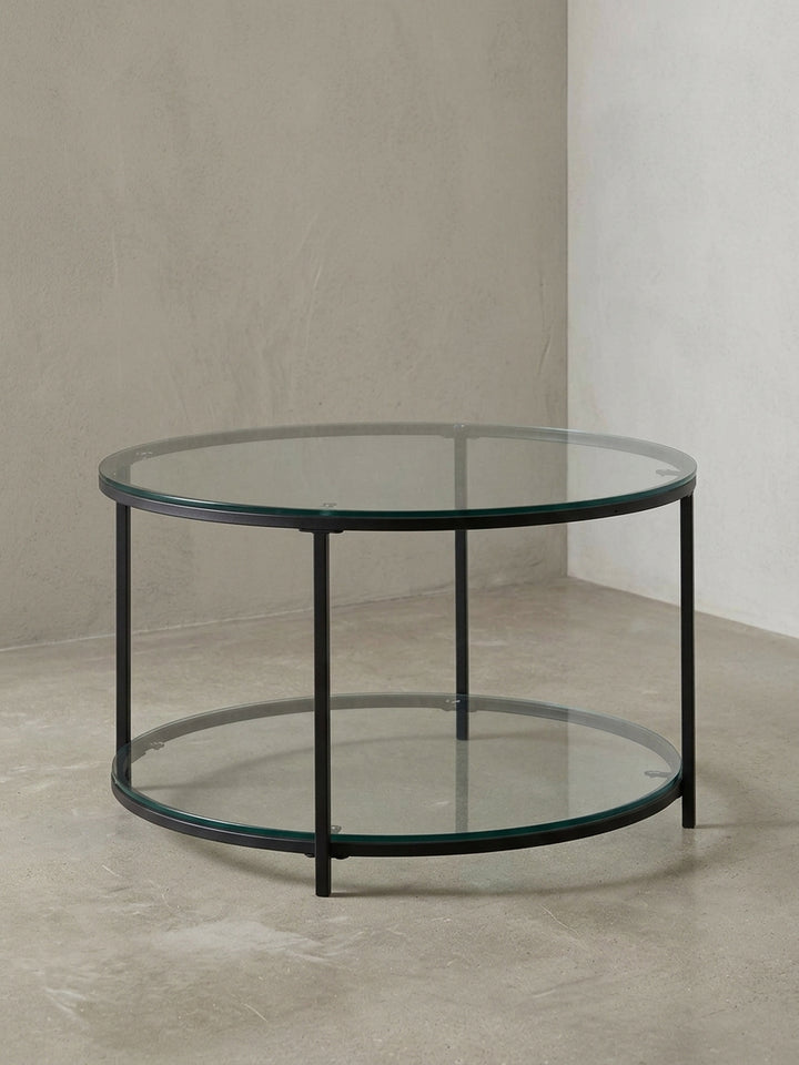 Runder Couchtisch mit zwei transparenten Glasplatten und einem filigranen, schwarzen Metallgestell, freigestellt vor weißem Hintergrund._