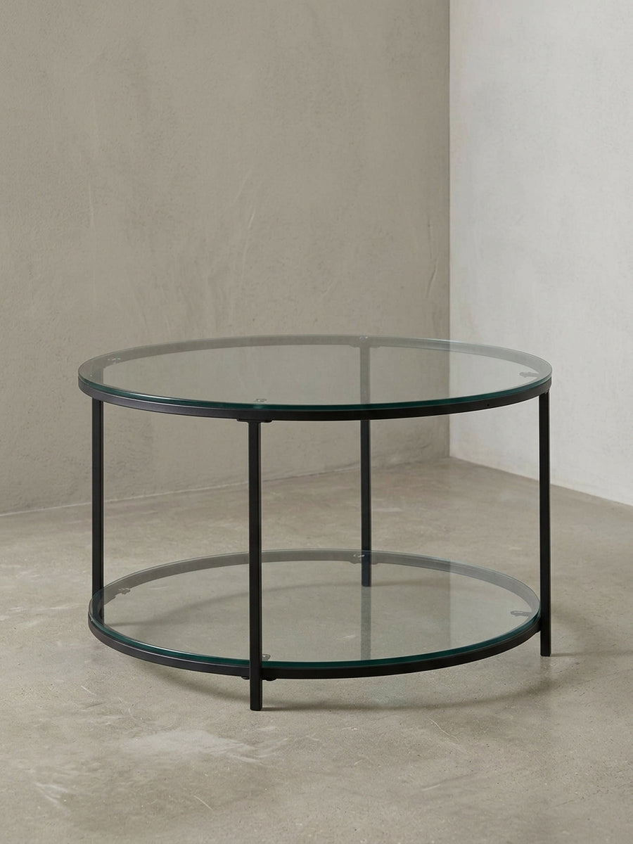 Runder Couchtisch mit zwei transparenten Glasplatten und einem filigranen, schwarzen Metallgestell, freigestellt vor weißem Hintergrund._