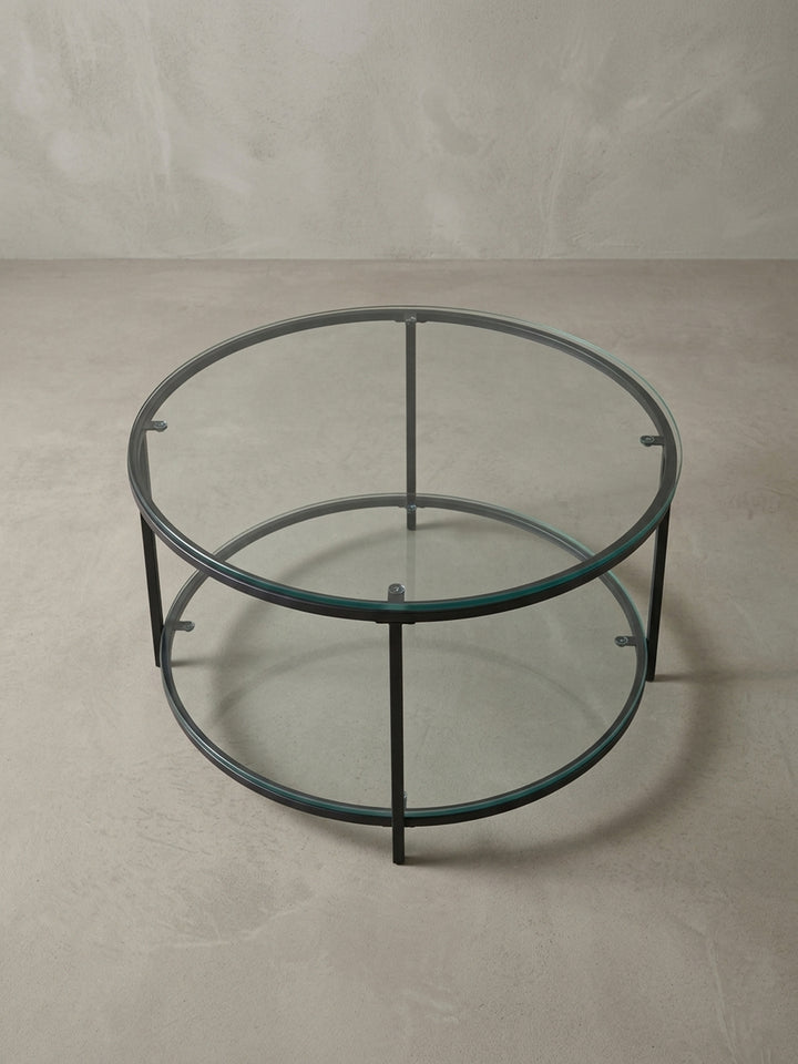 Minimalistischer Loungetisch mit 80 cm Durchmesser aus Glas und Stahl, aus einer leicht erhöhten Perspektive fotografiert, um die runde Form zu betonen._