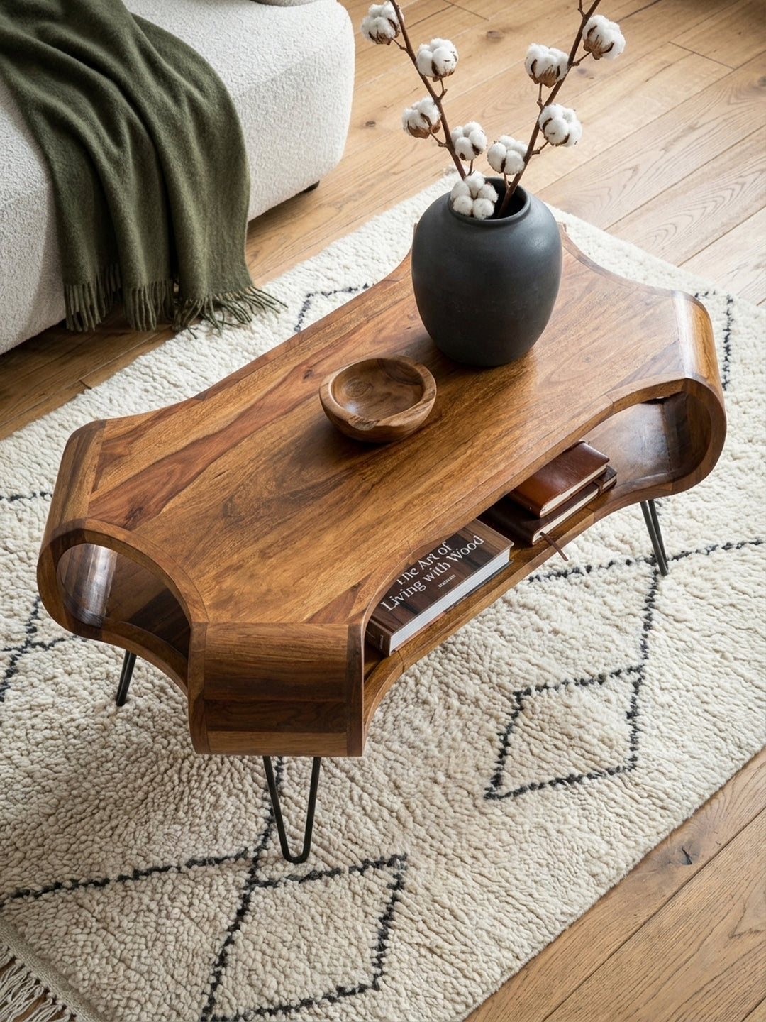 Draufsicht auf den Designer-Couchtisch aus Sheeshamholz auf einem Berberteppich, arrangiert mit einem L-Sofa und einem Ledersessel in einem großzügigen Altbau-Wohnzimmer._