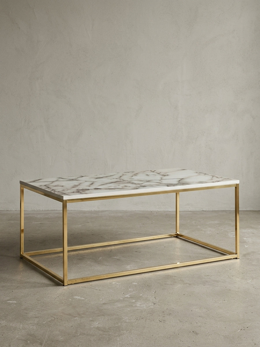 Moderner Couchtisch 100x60 cm freigestellt vor weißem Hintergrund, mit weißer Marmor-Optik Tischplatte und einem filigranen Gestell aus goldfarbenem Stahl._