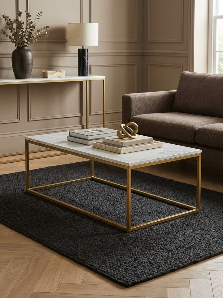 Draufsicht auf den 100x60 cm Couchtisch in Weiß-Gold, der mit Büchern und Dekoration auf einem strukturierten Teppich vor einem Sofa arrangiert ist._